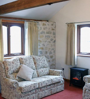 The lounge in the interior of Wagon House Holiday Cottages in the beautiful Vale of Glamorgan, Wales. Sofa and wood burner with large windows and lots of daylight. The converted holiday cottages are situated in a quiet village only 10 minutes walk from the sea